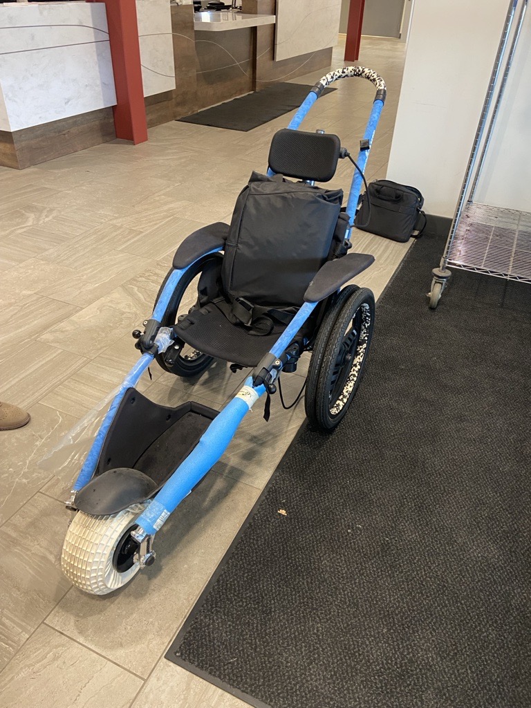 a bright blue aquatic wheelchair with three wheels, a black seat, black headrest and black arm rests.