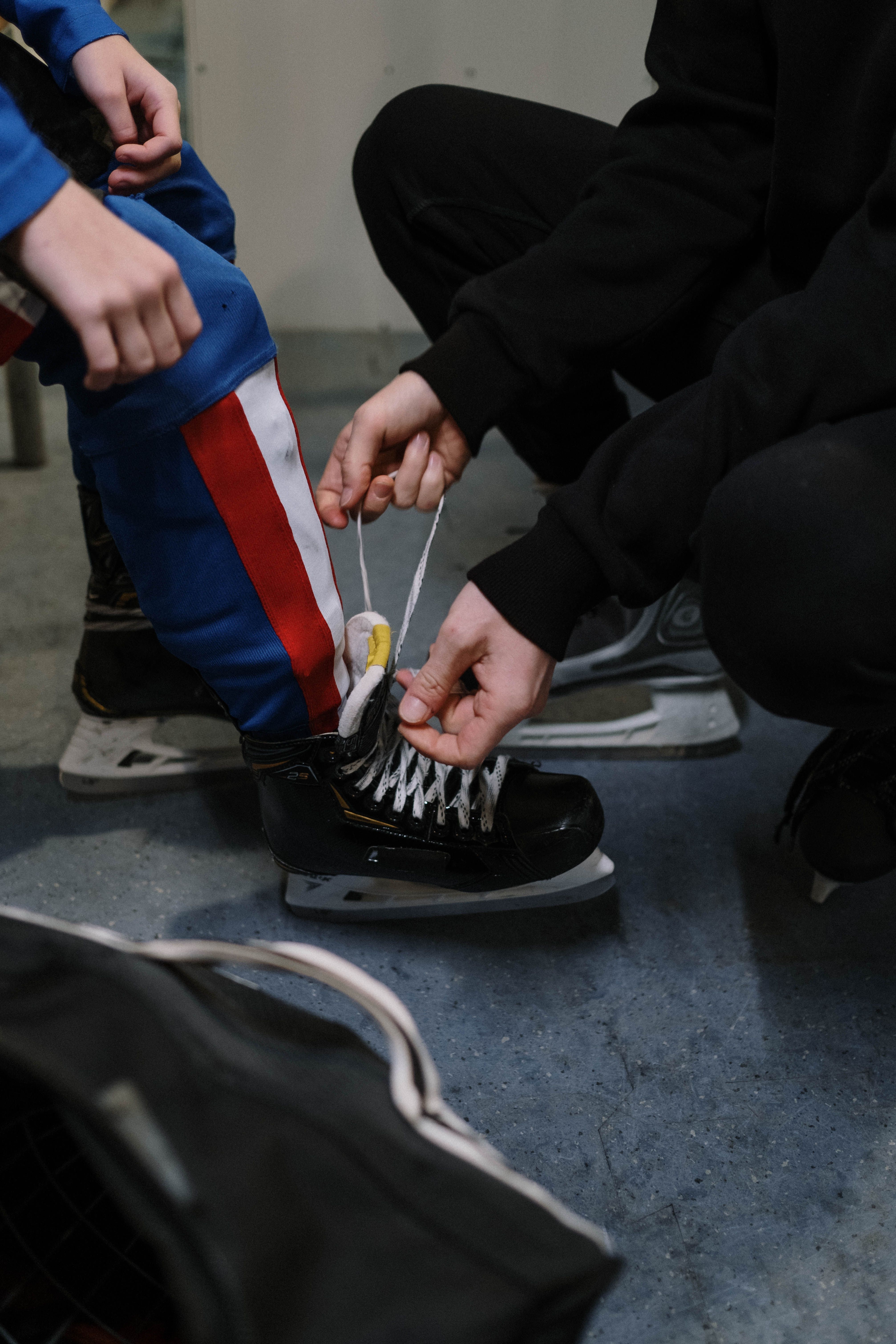 Photograph shows adult hands tying the laces of the hockey skates of a child.